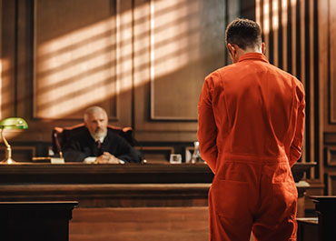 Man in orange jumpsuit facing a judge in a courtroom, symbolizing criminal charges and legal proceedings