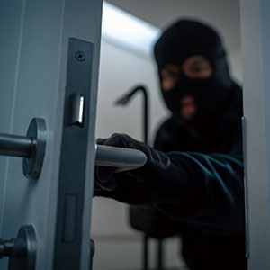Burglar with crowbar breaking into a home, symbolizing theft and criminal defense.