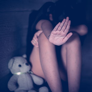 Child sitting with hand raised in fear, symbolizing abuse and need for legal protection and support.