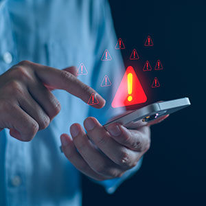 Person holding phone with warning signs, symbolizing digital fraud and cybercrime.