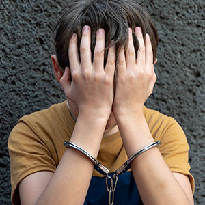 Child in handcuffs covering face, symbolizing juvenile crimes and legal defense.