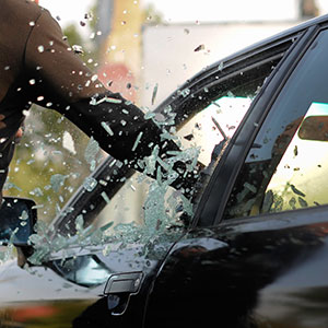 Person breaking car window, symbolizing auto theft and larceny legal defense.