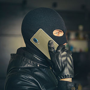 Masked person on phone, symbolizing threats, blackmail, and extortion crimes.