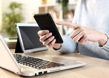 A person uses a smartphone while a laptop and tablet are on the desk.