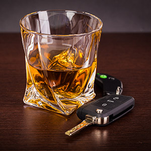 A twisted glass of amber liquor sitting next to a car key fob and a second key on a wooden surface, symbolizing DUI